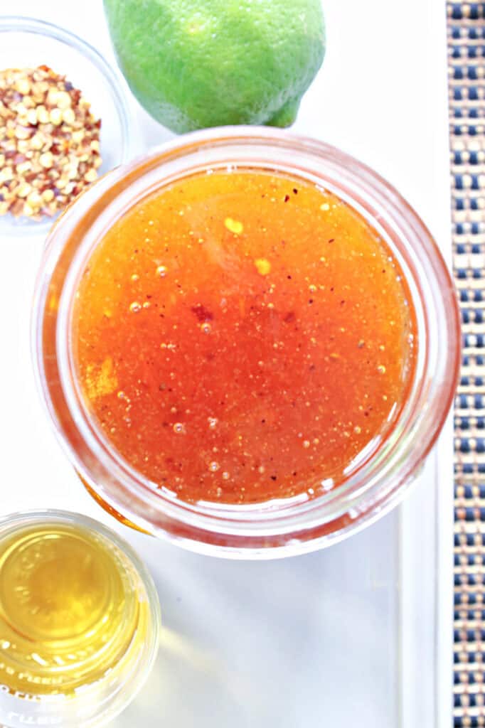 A vertical overhead closeup image of a mason jar filled with Irish Whiskey Glaze along with a fresh lime, red pepper flakes, and a shot glass of whiskey.