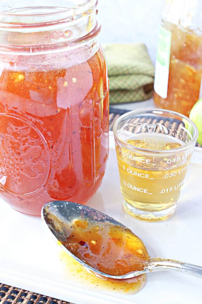 A closeup vertical image of Irish Whiskey Glaze in a mason jar along with a spoon and a shot glass filled with whiskey.