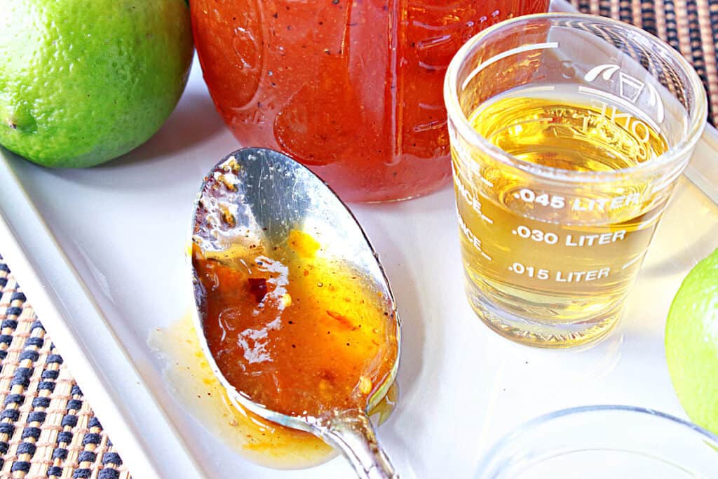 A closeup of a spoon that holding Irish Whiskey Glaze on a white plate with a shot glass of whiskey on the side.