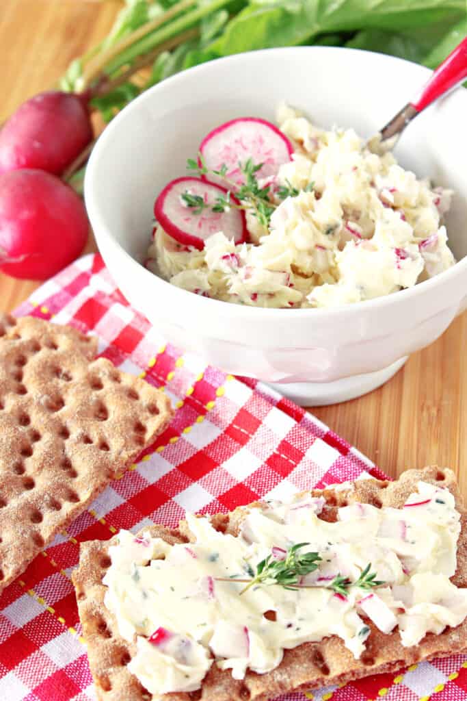 A vertical closeup of some Compound Radish Butter with Fresh Thyme in a small bowl and on a cracker.