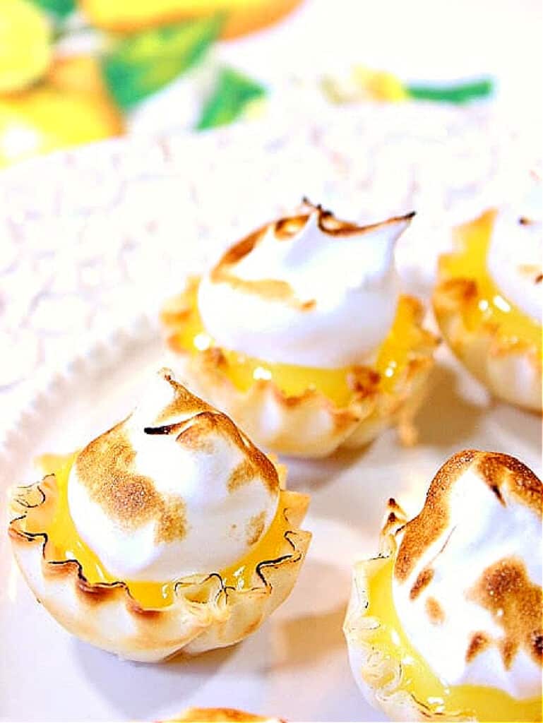 A super closeup photo of Lemon Meringue Tartlets on a white platter with toasted meringue toppings.