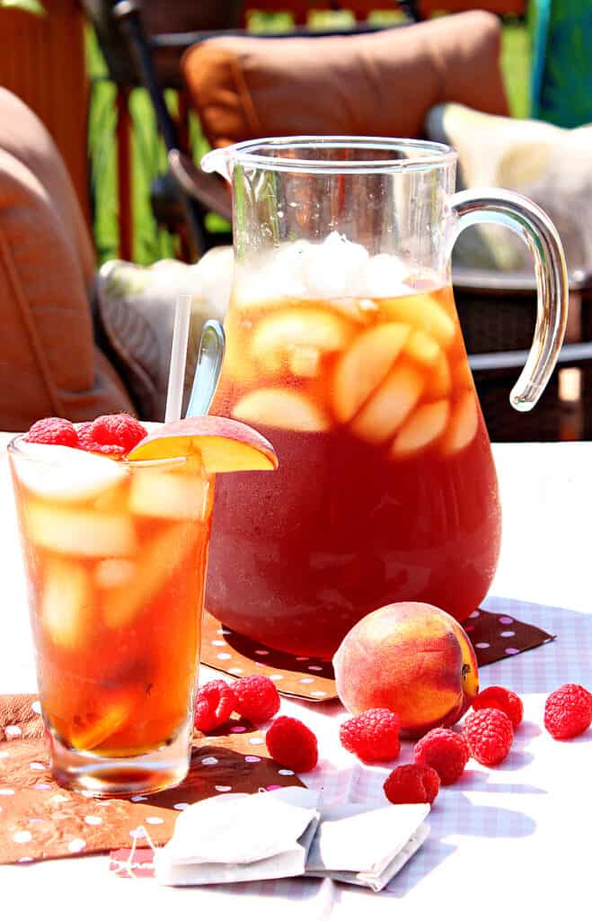 A pitcher and a glass of Peach and Raspberry Sun Tea outside with ice.