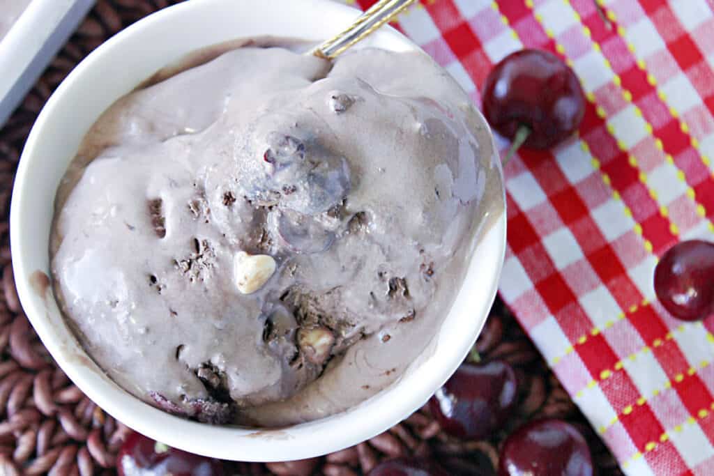 An offset overhead photo of a round white dish filled with melted Chocolate Cherry Kahlua Ice cream with a spoon.