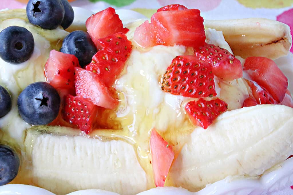 A horizontal closeup of a Frozen Greek Yogurt Banana Split topped with diced fresh strawberries, blueberries, and honey.