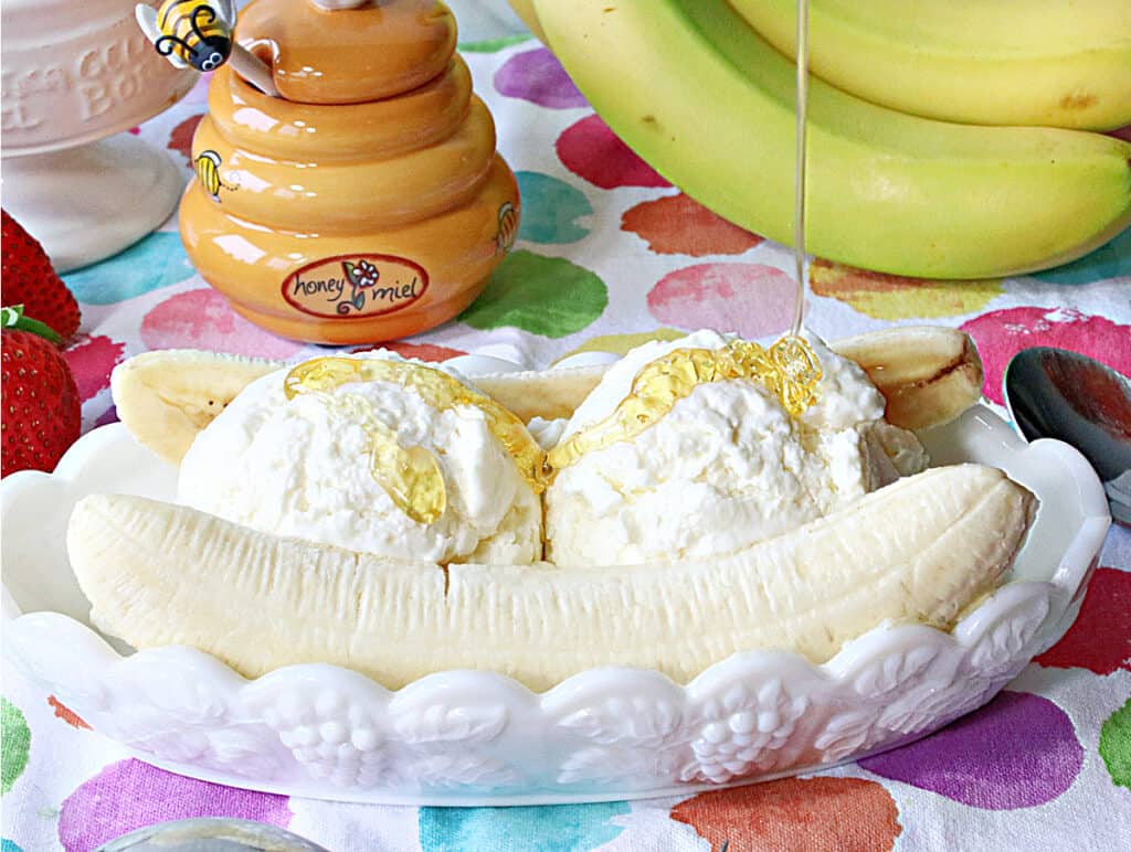 A closeup horizontal image of honey being drizzled onto a Frozen Greek Yogurt Banana Split with fresh bananas in the background.