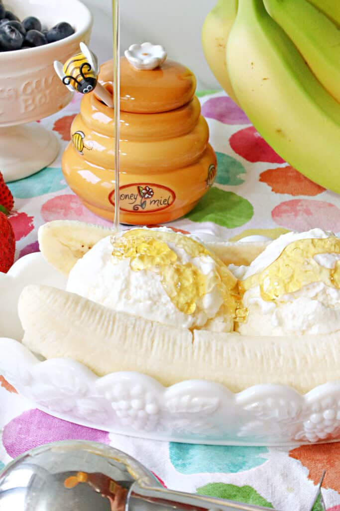 A closeup vertical image of a Frozen Greek Yogurt Banana Split being drizzled with honey.