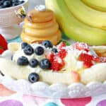 A white banana split dish filled with a Frozen Greek Yogurt Banana Split with blueberries and strawberries on top.