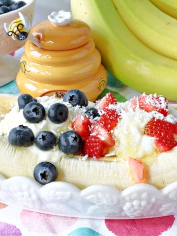 A white banana split dish filled with a Frozen Greek Yogurt Banana Split with blueberries and strawberries on top.