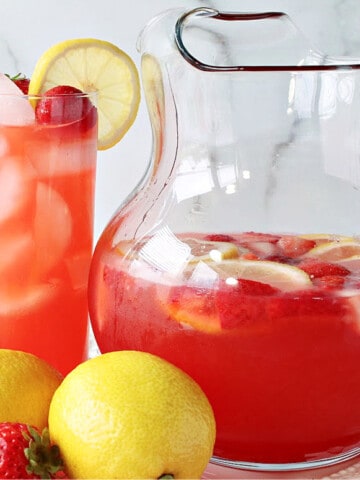 A glass and a pitcher filled with Lite Pink Lemonade with Strawberry Simple Syrup.