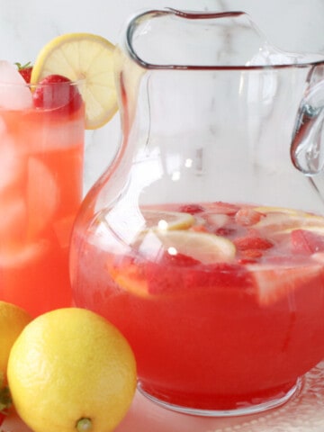 A pitcher and a glass of Lite Pink Lemonade with ice and citrus.