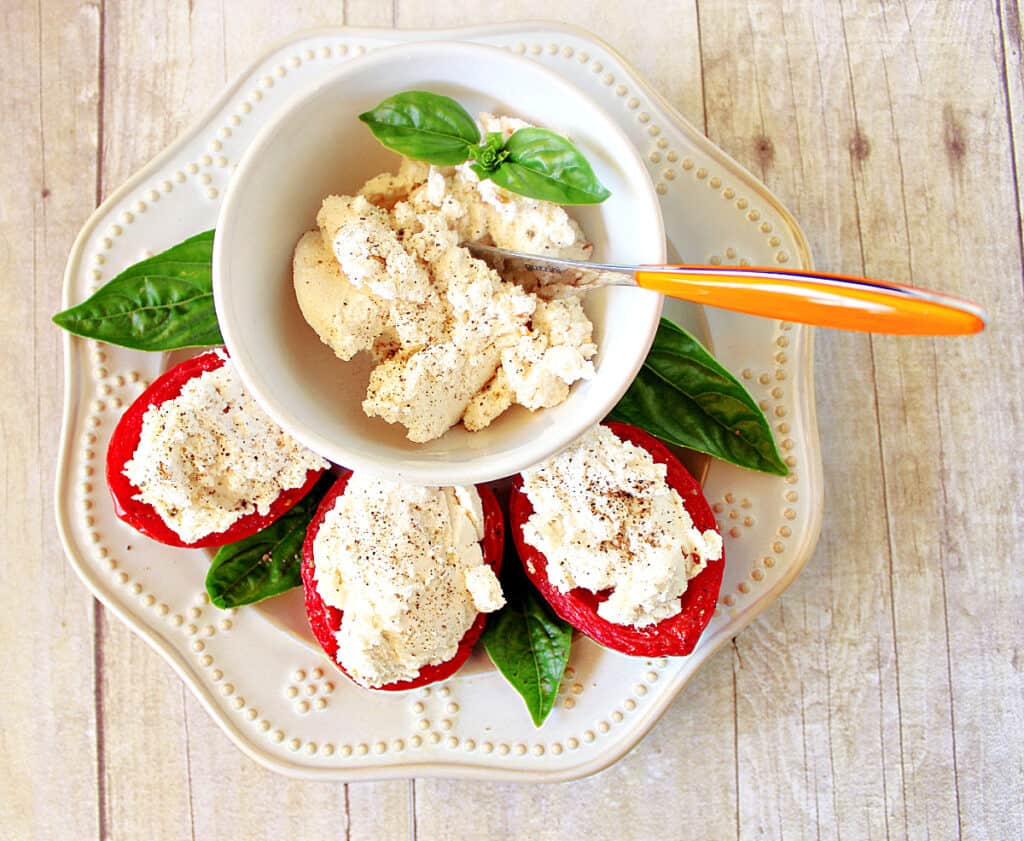 A direct overhead photo of Homemade Red Pepper Ricotta Cheese stuffed into Roasted Roma Tomatoes along with fresh basil leaves as garnish.