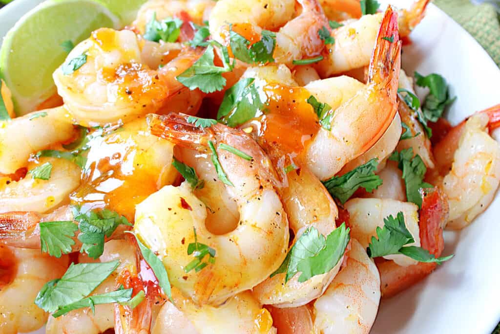 A super closeup horizontal photo of Whiskey Glazed Roasted Shrimp with chopped cilantro and lime wedges.