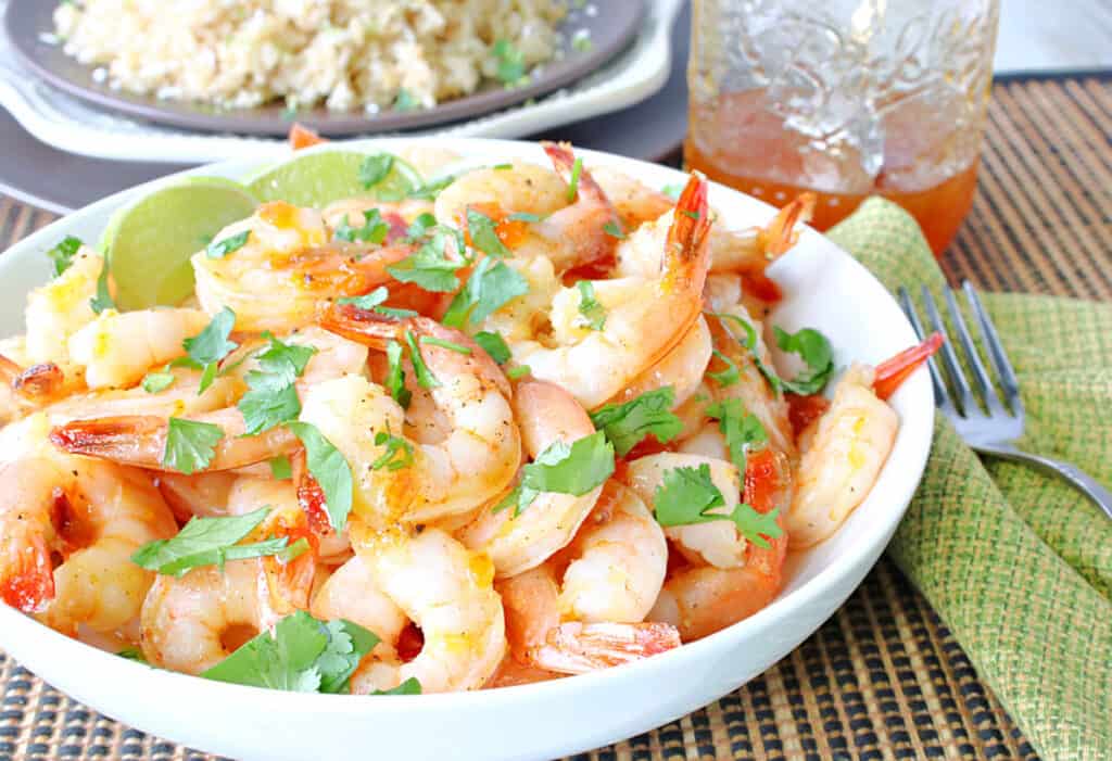 A white bowl filled with Whiskey Glazed Roasted Shrimp along with a jar of whiskey glaze in the background.