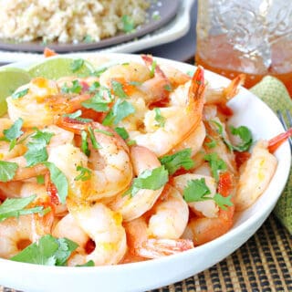A white bowl filled with Whiskey Glazed Roasted Shrimp along with a jar of whiskey glaze in the background.