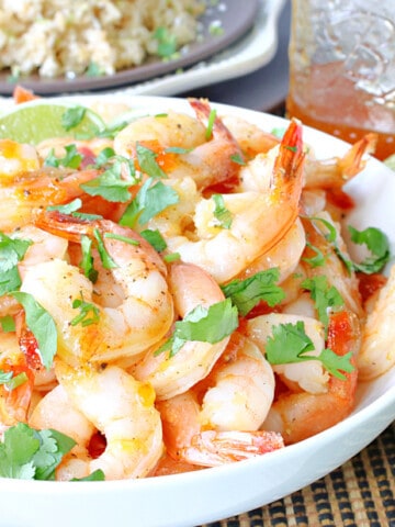 A white bowl filled with Whiskey Glazed Roasted Shrimp along with a jar of whiskey glaze in the background.