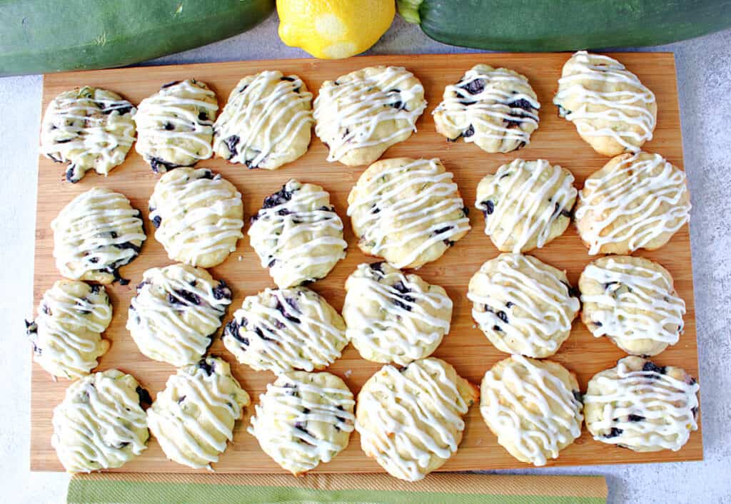 A directly overhead photo of a wooden tray filled with Zucchini Ricotta Cookies with a lemon buttercream icing drizzle.