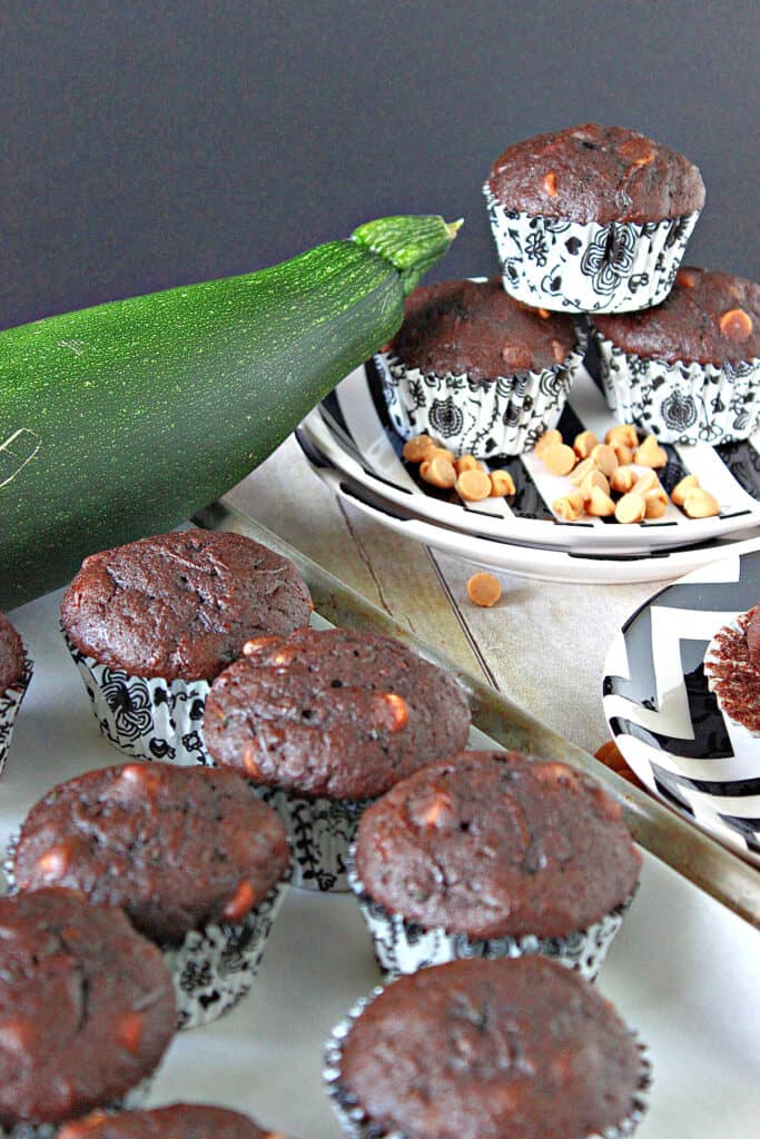 A vertical image of Chocolate Zucchini Muffins with Peanut Butter on a baking sheet in the foreground and a plate with muffins in the background.