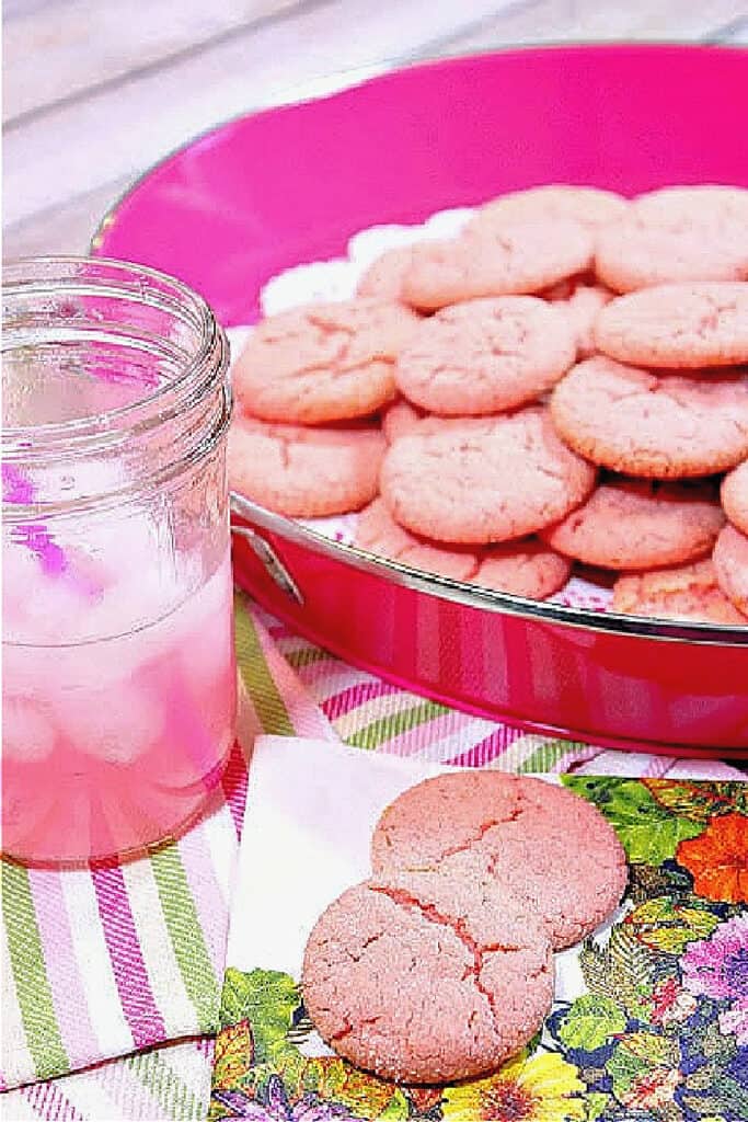 A pink tray filled with Pink Lemonade Cookies along with a glass of pink lemonade on the side with ice.