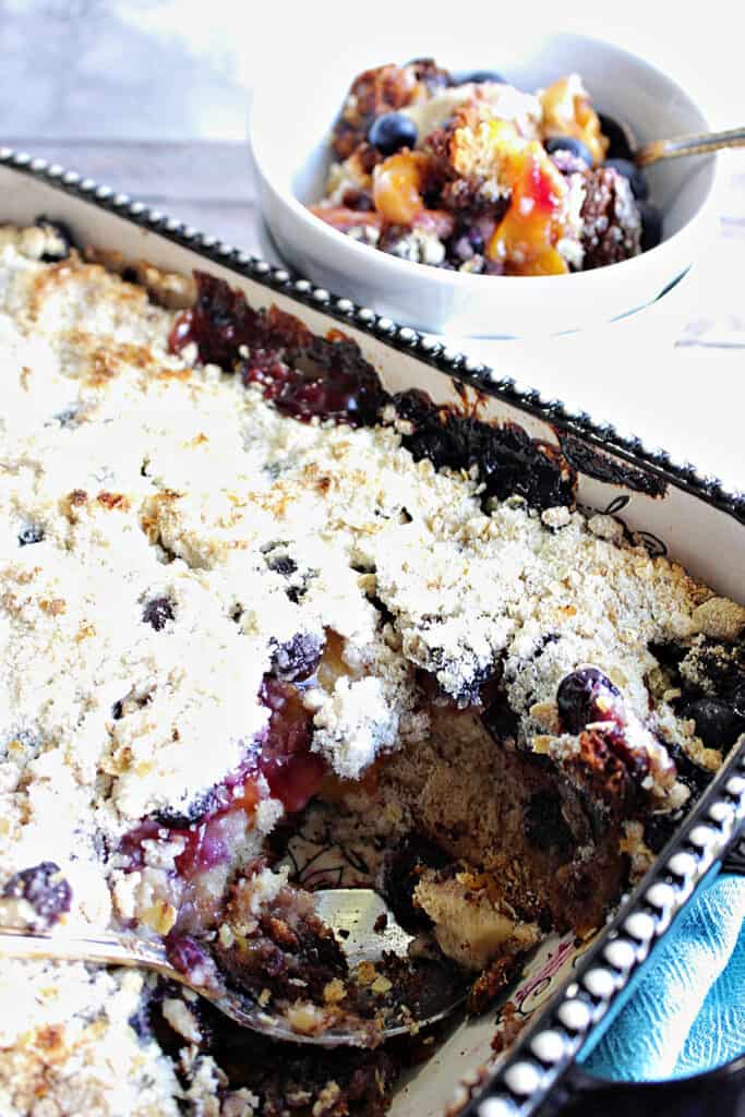 A vertical closeup of a rectangle baking dish filled with Blueberry Peach Crisp along with a small dish of crisp in the background.