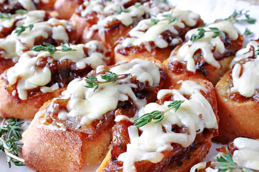 A closeup photo of French Onion Crostini on a plate with melted cheese and fresh thyme sprigs on top.