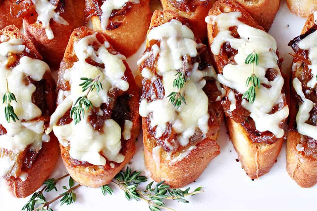 A row of French Onion Crostini on a white platter with melted cheese and fresh thyme.