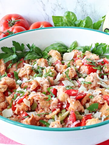 A large serving bowl filled with Italian Panzanella Salad topped with fresh basil and cheese.