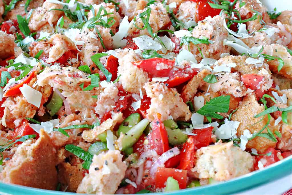 A closeup horizontal photo of an Italian Panzanella Salad topped with fresh tomatoes, fresh basil, and fresh Parmesan cheese.