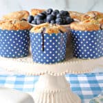 A white cake stand filled with some NY Times Blueberry Muffins in blue and white polka dot cups.