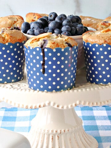 A white cake stand filled with some NY Times Blueberry Muffins in blue and white polka dot cups.