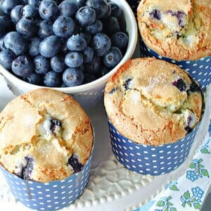 Blueberry muffins in blue and white polka dot cups along with a bowl of fresh blueberries.