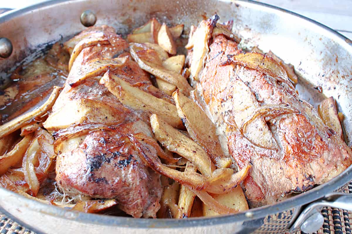 Two glazed pork tenderloin in a skillet with cinnamon apples and onions.
