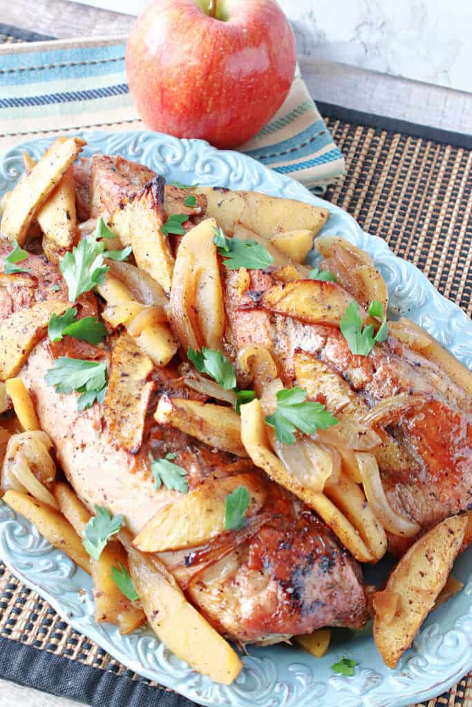 A pretty blue platter filled with skillet pork tenderloin with apples and onions.