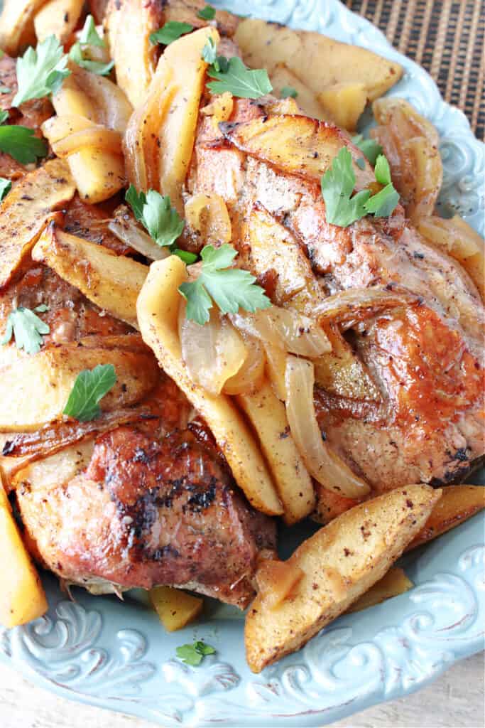 A super closeup overhead photo of a Skillet Pork Tenderloin on a blue platter along with cinnamon apples and onions.