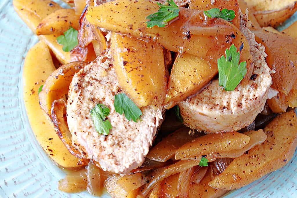 A super closeup of slices of Skillet Pork Tenderloin topped with cinnamon apples on a blue plate with a parsley garnish.