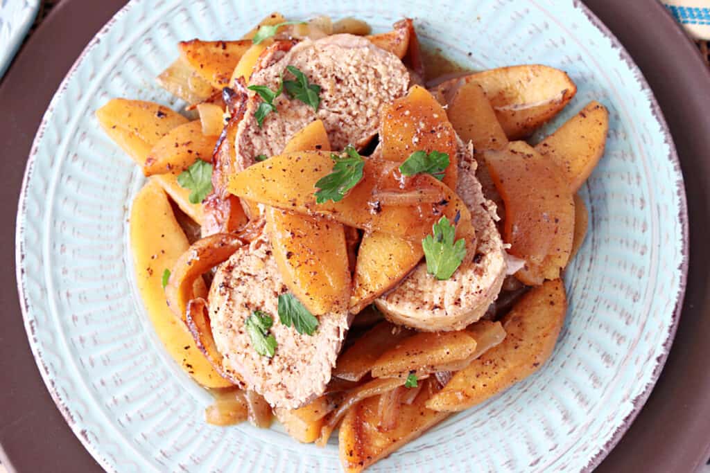 An overhead look at a dinner plate with pork slices and cooked apples.