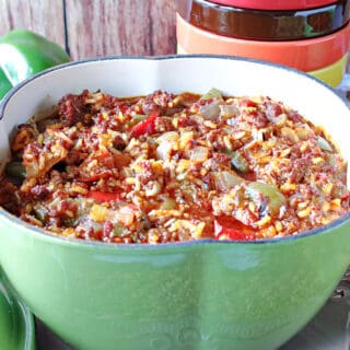 A green pepper shaped pot of Stuffed Green Pepper Stew along with some fresh green peppers in the background.