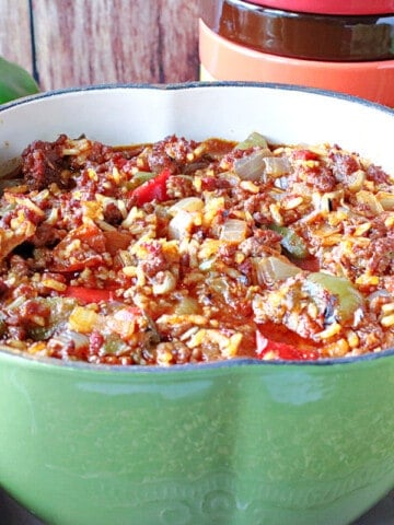 A green pepper shaped pot of Stuffed Green Pepper Stew along with some fresh green peppers in the background.