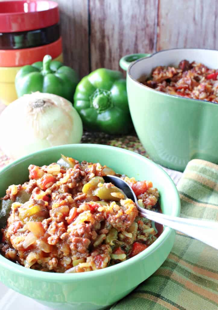 A vertical closeup of a bowl of Stuffed Green Pepper Stew in the foreground along with a casserole dish filled with stew in the background.