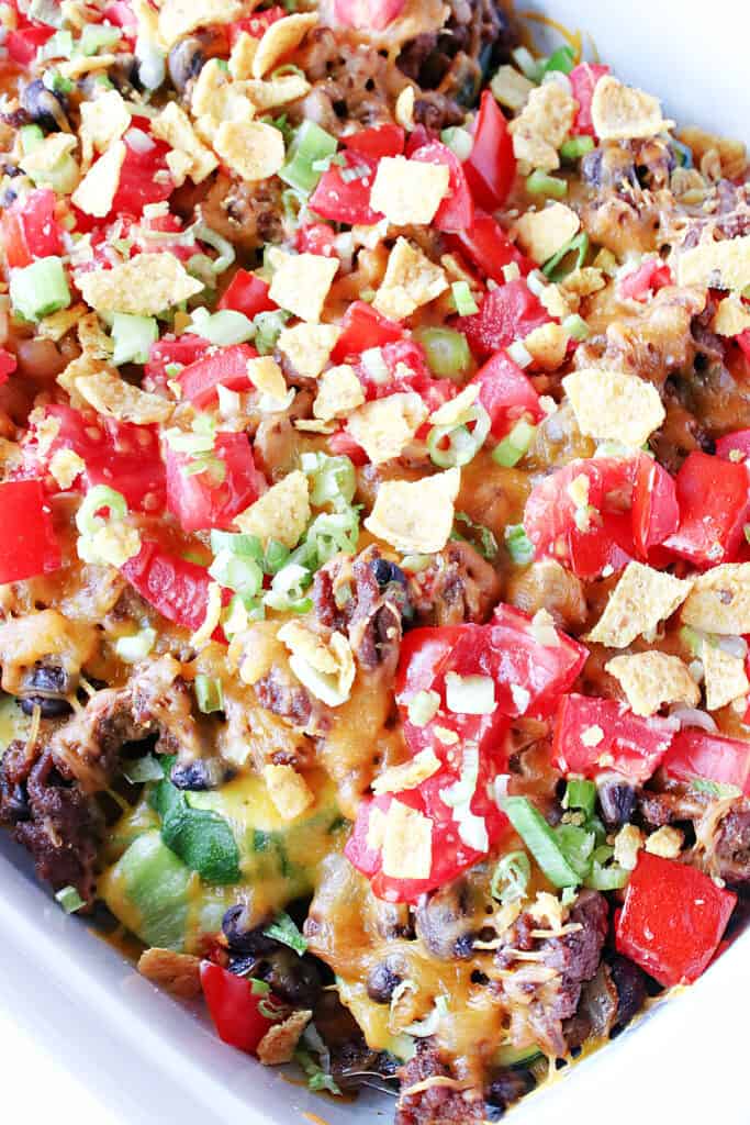 A super closeup vertical image of Taco-Filled Zucchini Boats with chopped tomatoes, cheddar cheese, scallions, and corn chips.