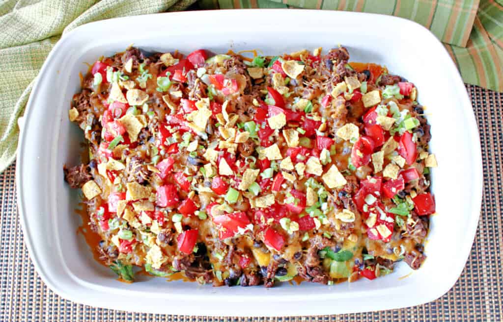 A direct overhead photo of a white casserole dish filled with Taco-Filled Zucchini Boats with tomatoes, green onions, ground beef and cheese.