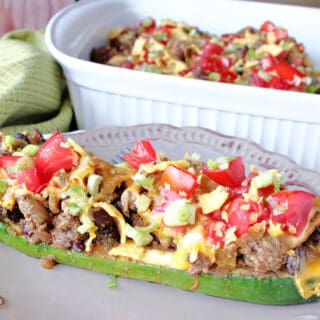 A Taco-Filled Zucchini Boat filled with ground beef, tomatoes, cheese, and beans in the foreground with a casserole dish in the background.