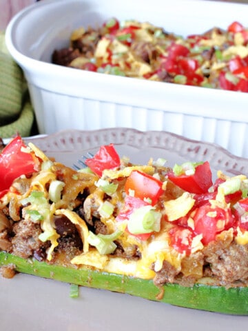 A Taco-Filled Zucchini Boat filled with ground beef, tomatoes, cheese, and beans in the foreground with a casserole dish in the background.