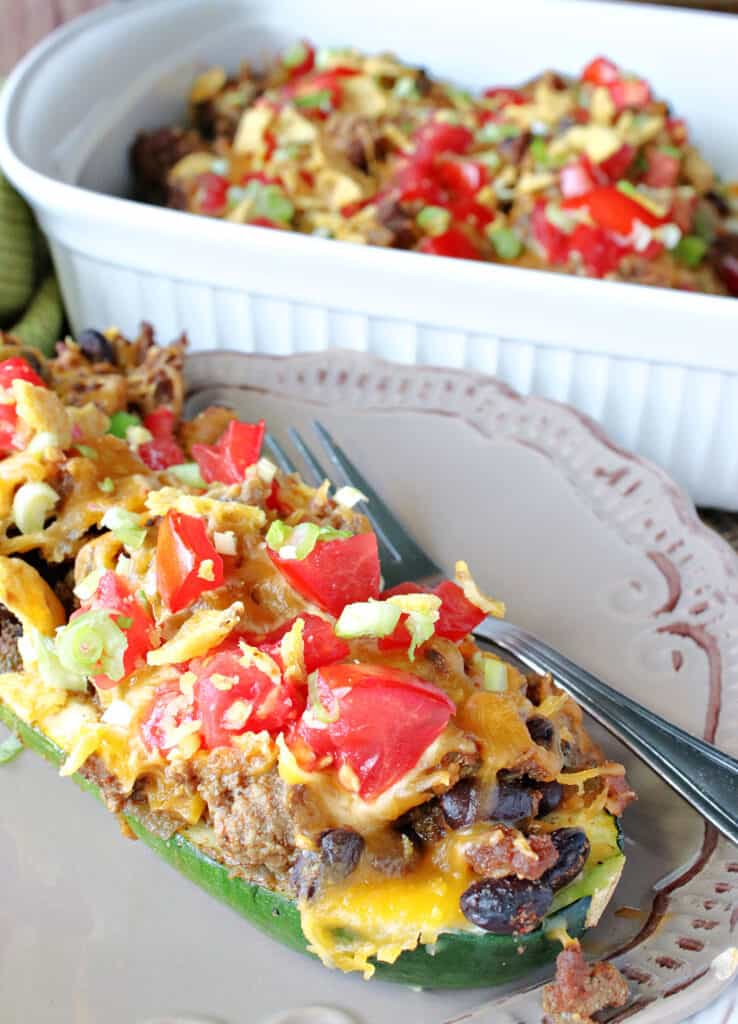 A closeup vertical photo of Taco Filled Zucchini Boats on a plate with a casserole dish in the background.