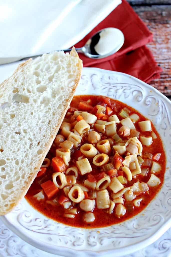 A bowl of hearty Tuscan Pasta Soup in a white bowl with napkins and a spoon in the background.