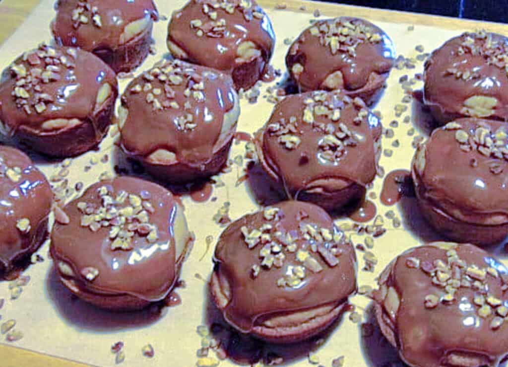 A closeup horizontal photo of Caramel Apple Cupcakes topped with chopped pecans all lined up on a wooden board.