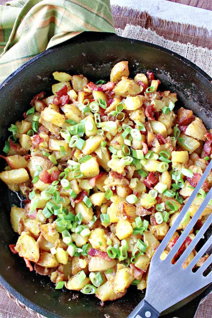 A vertical overhead photo of German Fried Potatoes in a cast iron skillet along with scallions for garnish.