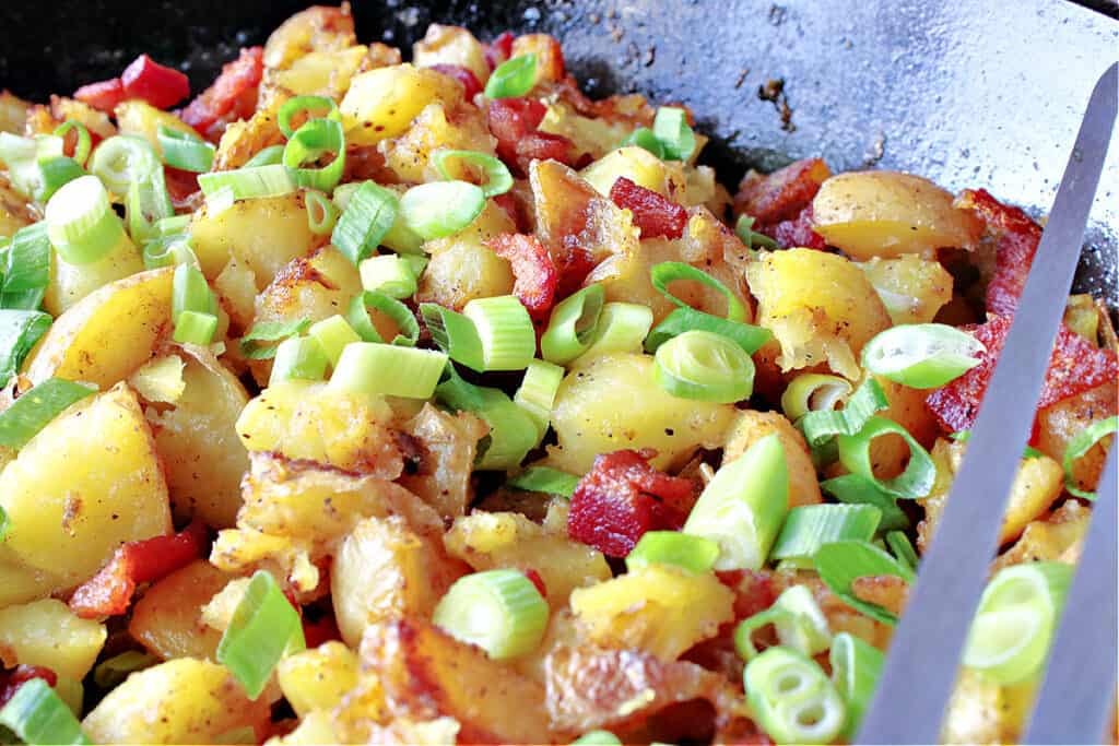 A horizontal closeup of German Fried Potatoes in a cast iron skillet along with bacon and scallions.