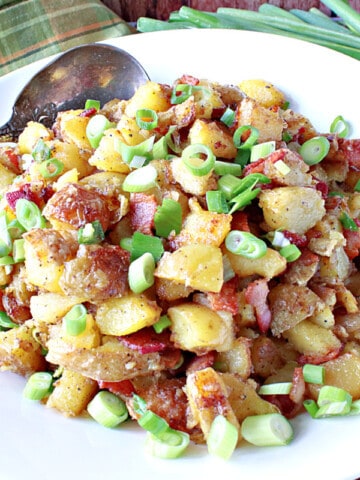 A white bowl filled with German Fried Potatoes along with scallions and a spoon.