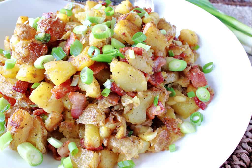 An offset horizontal photo of German Fried Potatoes in a white bowl topped with bacon and scallions. 