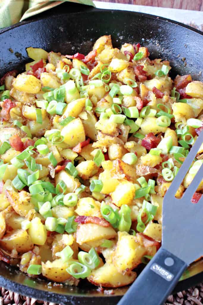 A vertical closeup of a cast iron skillet filled with German Fried Potatoes along with bacon and scallions.